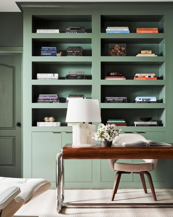 A stylish office space featuring sage green cabinets, light walls, and gold accents