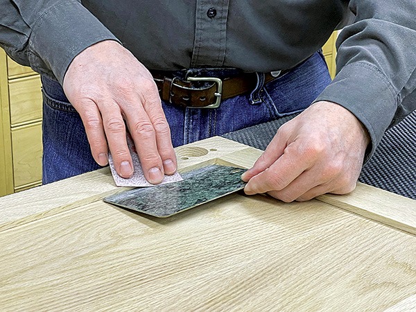 Craftsman manually sanding and finishing cabinet door edges