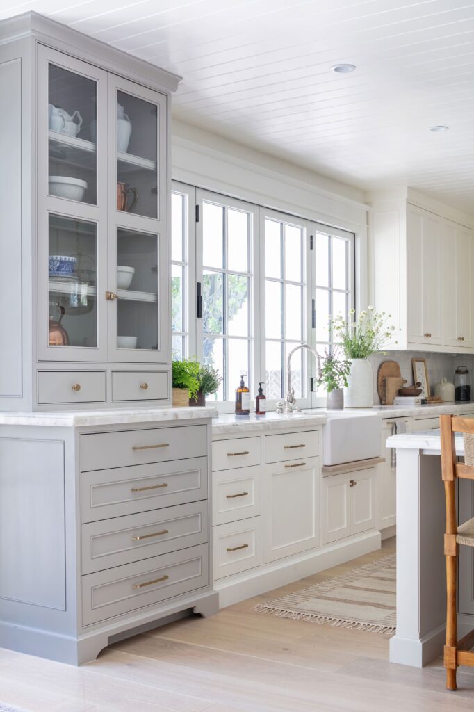 Minimalist kitchen with matte white and light gray cabinets, featuring brushed metal handles and marble backsplash
